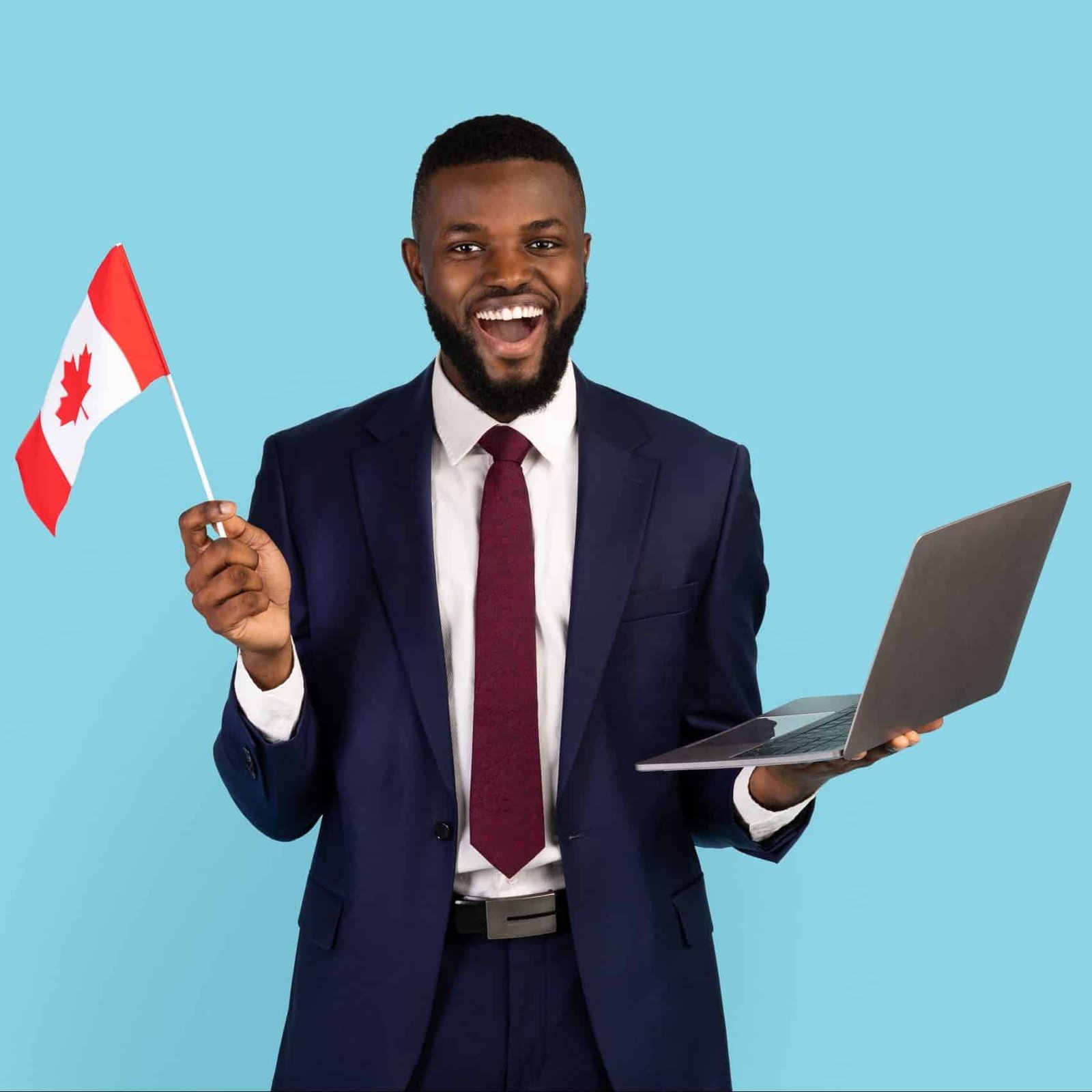 Excited Black Businessman In Suit With Canadian Flag And Laptop Posing Over Blue Studio Background, Joyful African American Male Entrepreneur Enjoying International Partnership And Online Study